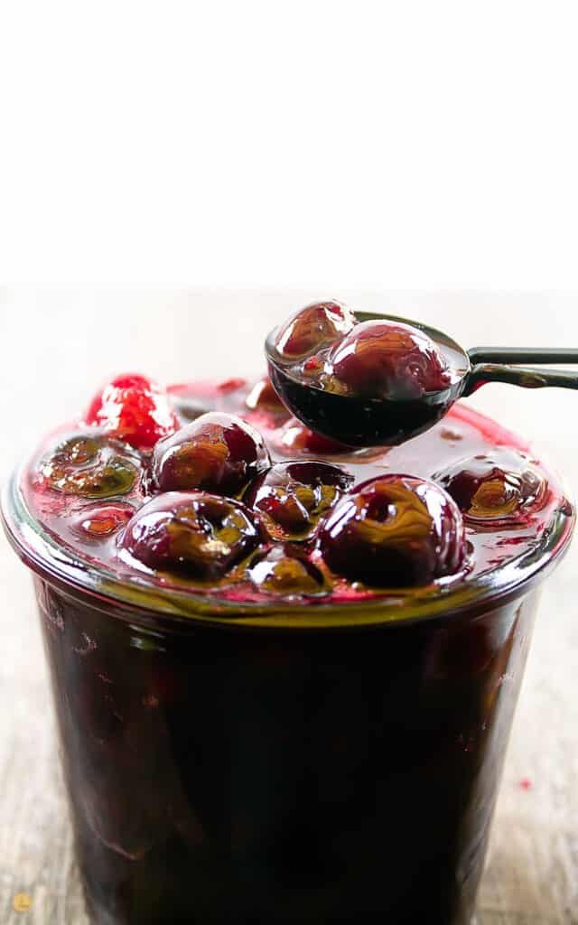 jar of cherry pie filling with a black measuring spoon scooping out some of the filling