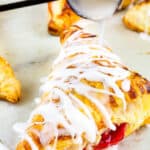 black spoon drizzling icing on a baked turnover on a baking sheet