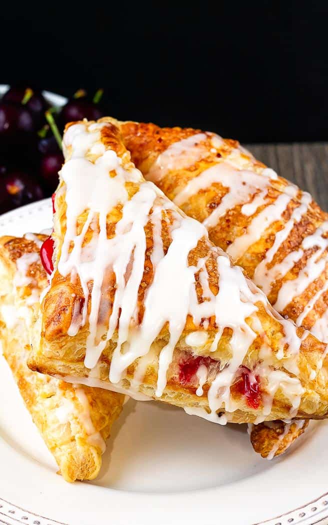 three cherry turnovers, drizzled with icing, on a white cake plate