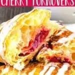 closeup of three turnovers cut in half on a wood cake stand with a white bowl of cherries behind it with text "puff pastry cherry turnovers"