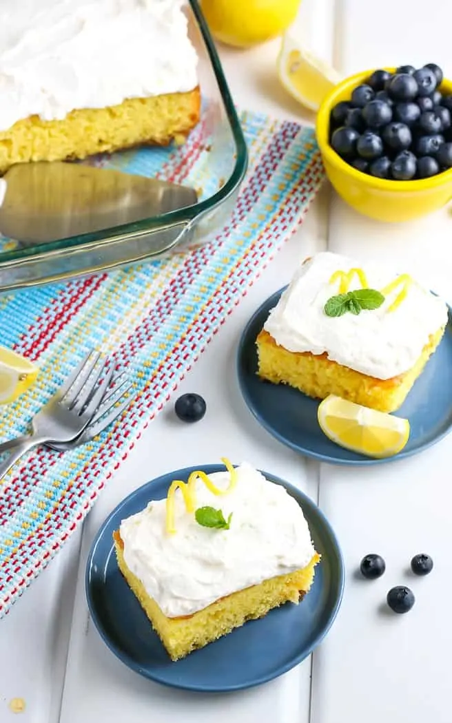 side angle of cake with two pieces cut and placed on small blue plates with bowl of blueberries next to it