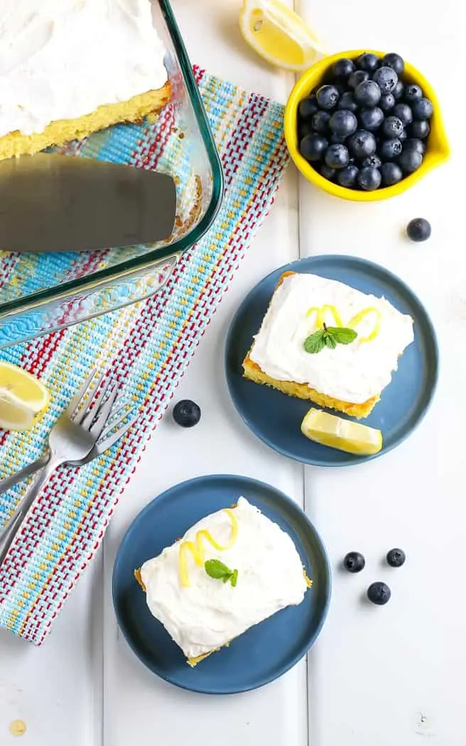 yellow cake with two pieces cut and placed on small blue plates with bowl of blueberries next to it