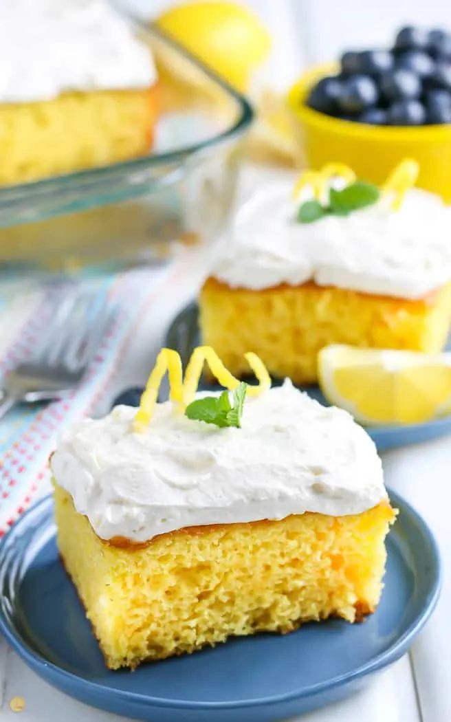 square of lemonade cake on a blue plate with mint garnish. other cake slices in the background.