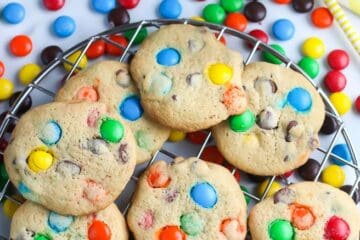 overhead picture of cookies with M and M candy on cooling rack with two glasses of milk and yellow straw