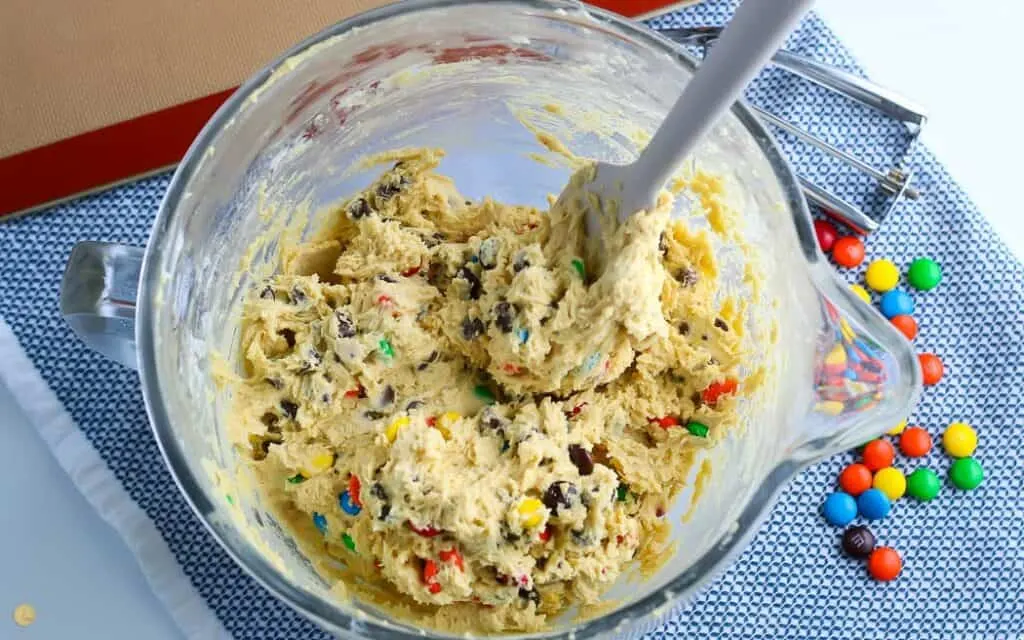 mixed M&M cookie dough in a clear mixing bowl on a blue placemat