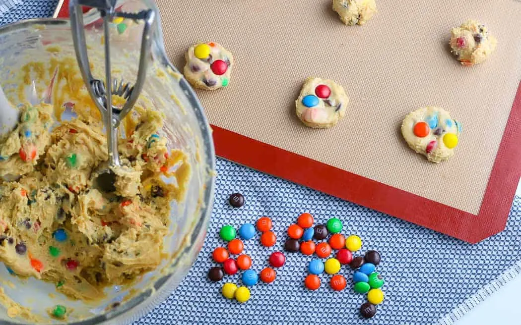 baking sheet with balls of cookie dough on it next to a mixing bowl with dough in it