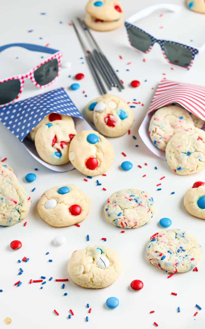 overhead picture of patriotic cookies with m&ms and sprinkles spread out with sprinkled in between and some sparklers in the background