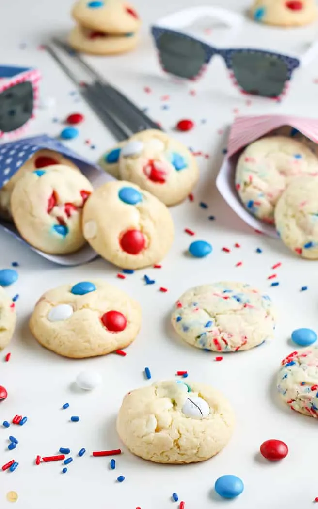 side angle picture of patriotic cookies with m&ms and sprinkles spread out with sprinkled in between and some sparklers in the background