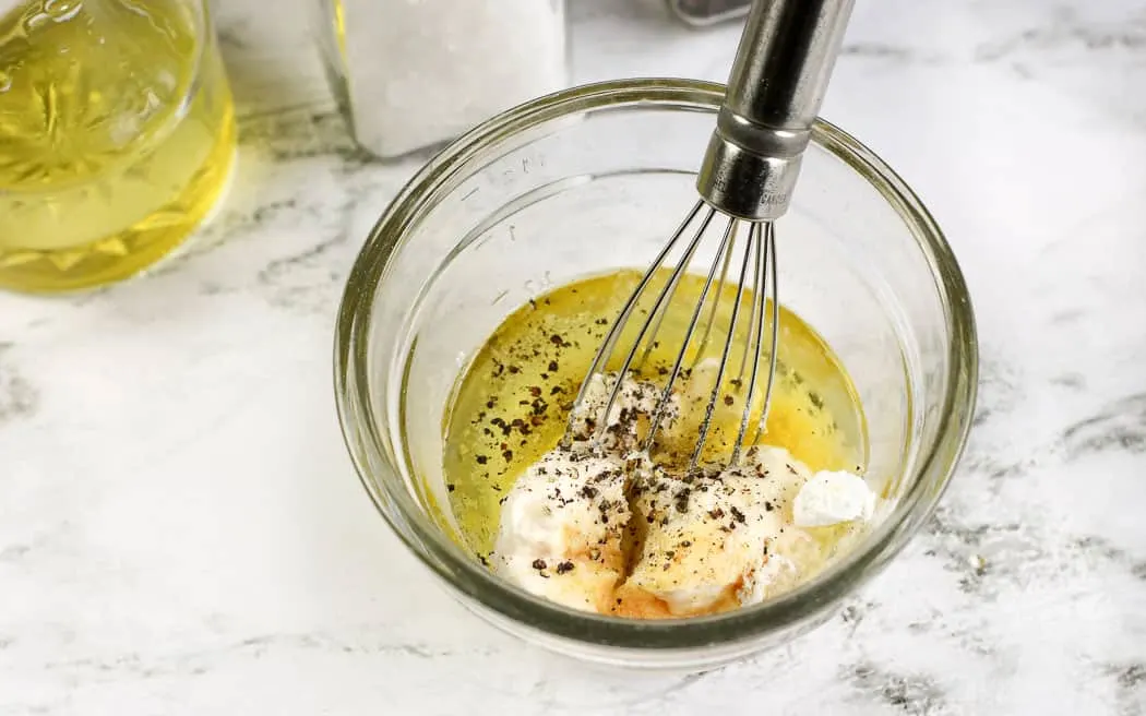 dressing ingredients unmixed in a clear bowl with a metal whisk in it