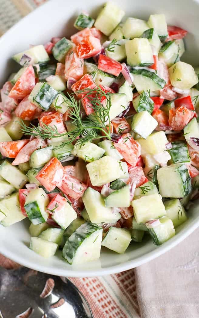 close up overhead picture of cucumber tomato dill salad in a white bowl with a spoon on the left