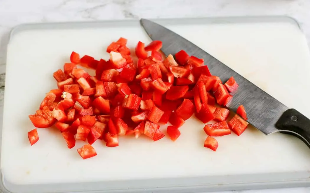 diced red bell pepper on a white cutting board with a knife