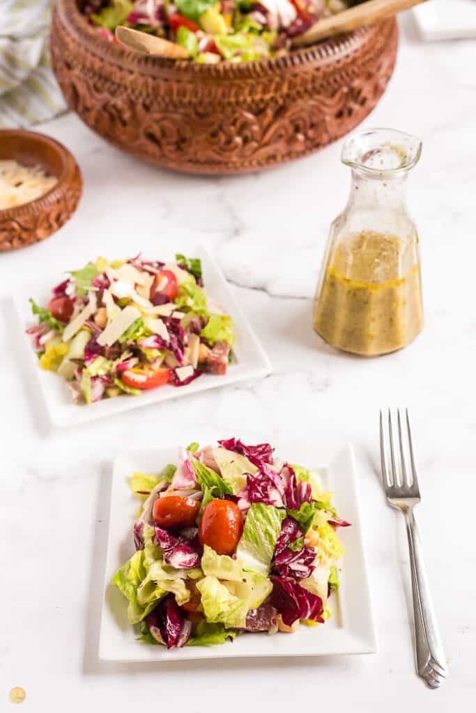 two side salads with forks on the plates and a bottle of salad dressing to the right