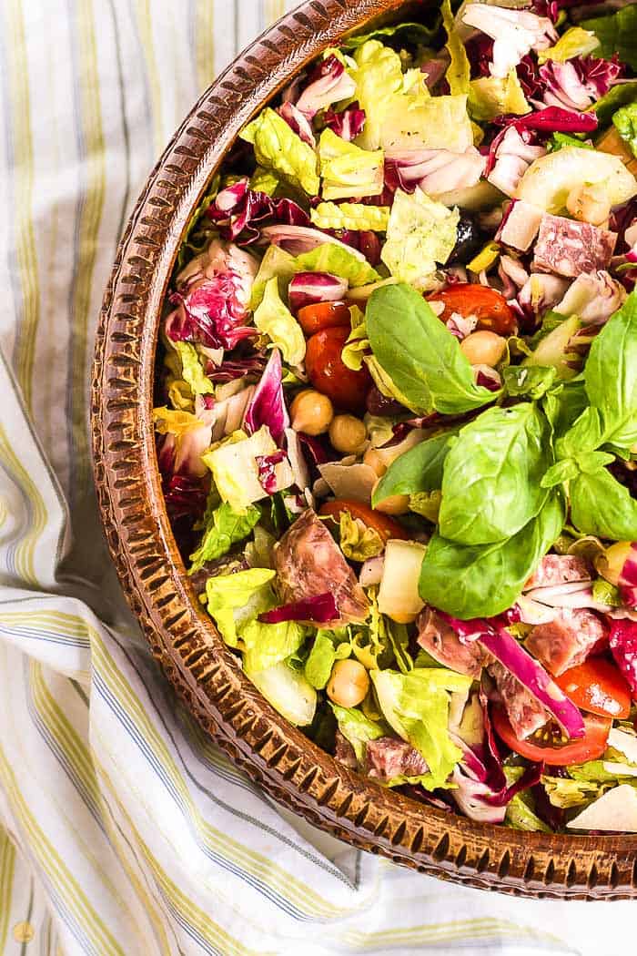 side photo of chopped salad in a wood bowl topped with basil leaves