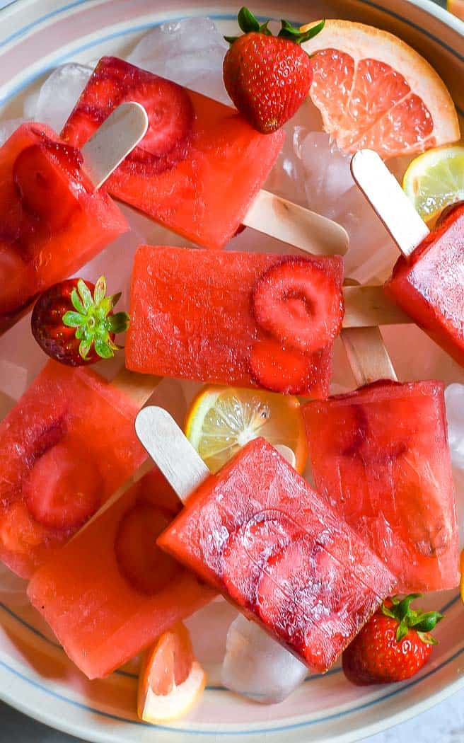 strawberry popsicles in a bowl of ice with grapefruit wedges and lemon slices