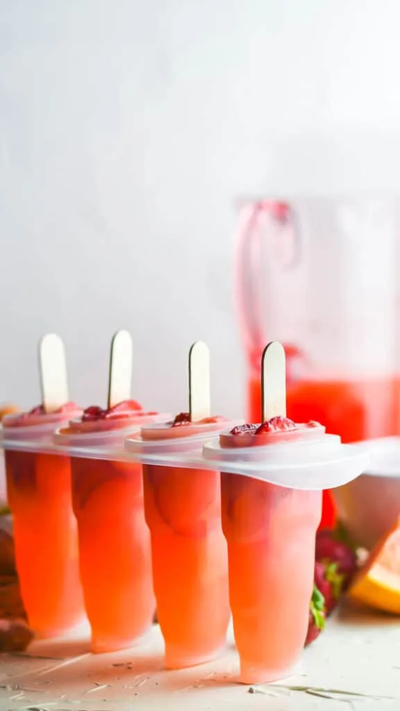 set of 4 popsicles in molds with a jar of strawberry juice behind it
