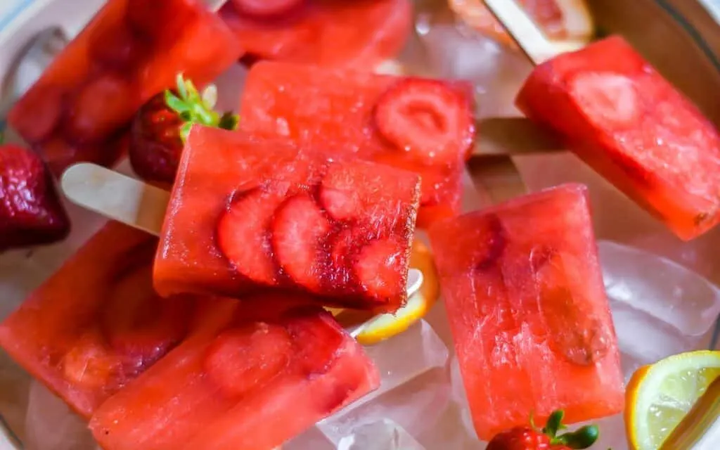 fresh fruit popsicles in a bowl of ice with lemon slices and whole strawberries