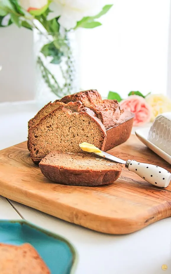 sliced banana bread loaf with butter on a spreader on a wood cutting board