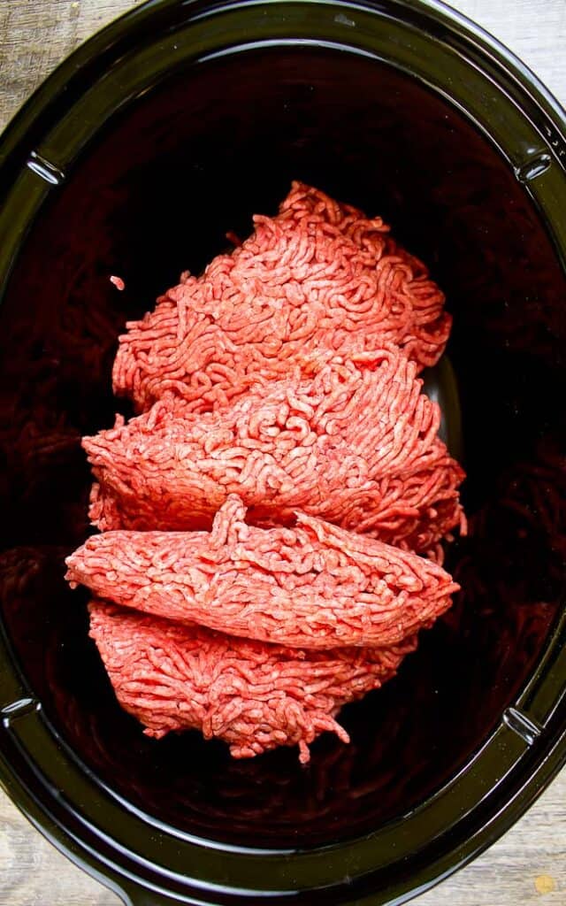 raw ground beef in a black crock pot bowl