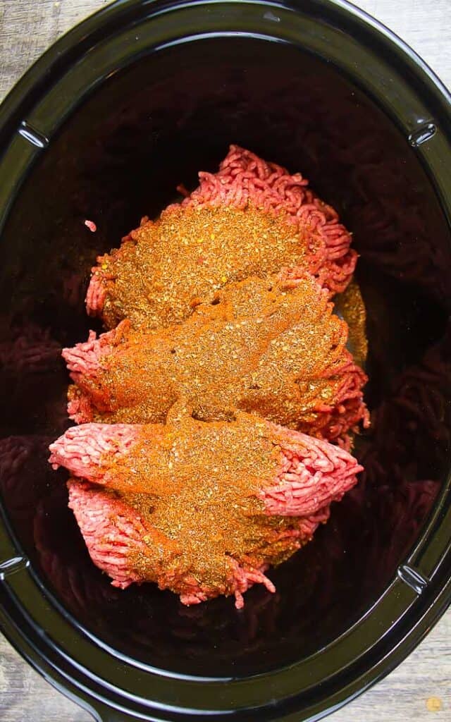 ground beef covered in taco seasoning in crock pot bowl