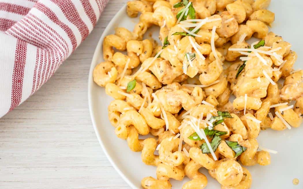 overhead picture of chicken pasta on white plate with red stripe napkin