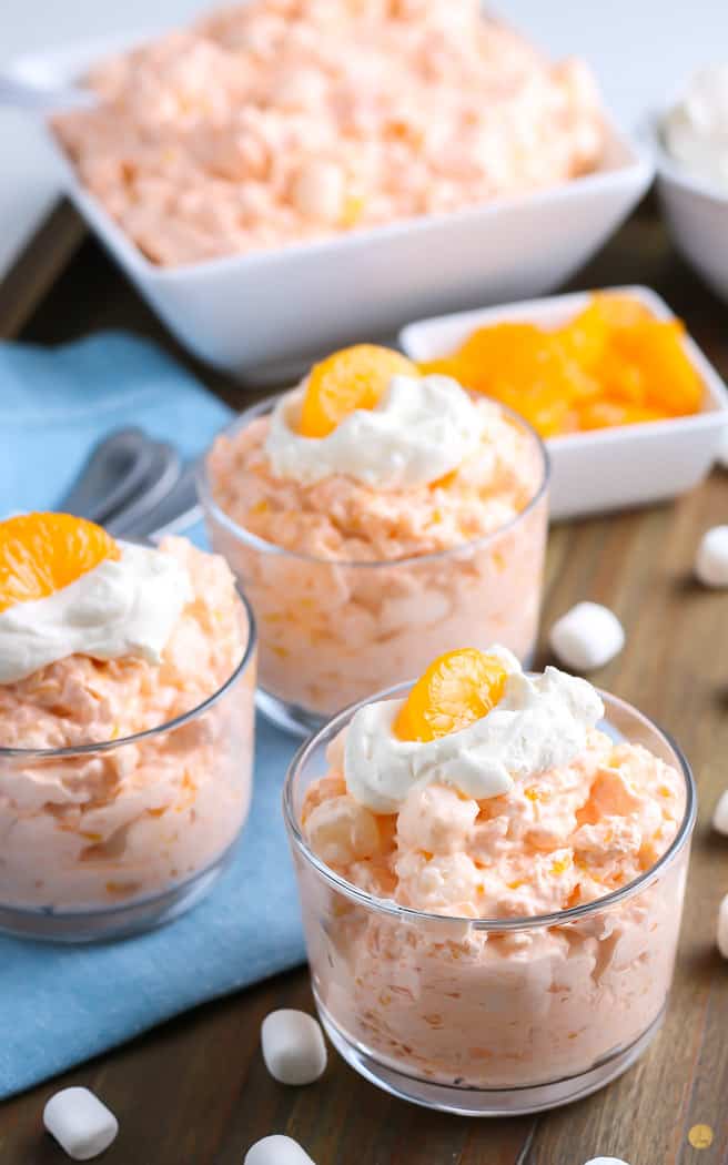 three small clear bowls with orange jello salad topped with orange slice