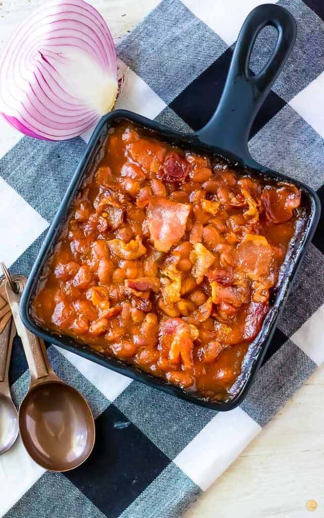 overhead picture of beans in a square pan on a checkerboard napkin with measuring spoons on the side