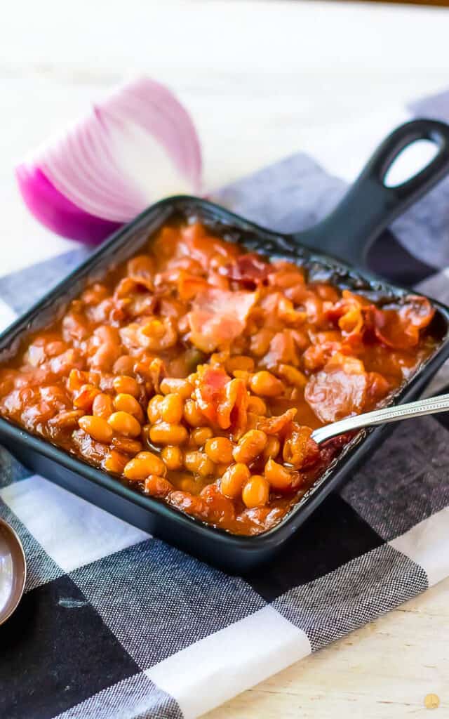 spoon scooping beans out of a square pan on a checkerboard napkin