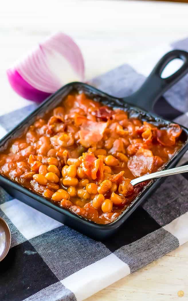 spoon scooping beans out of a square pan on a checkerboard napkin