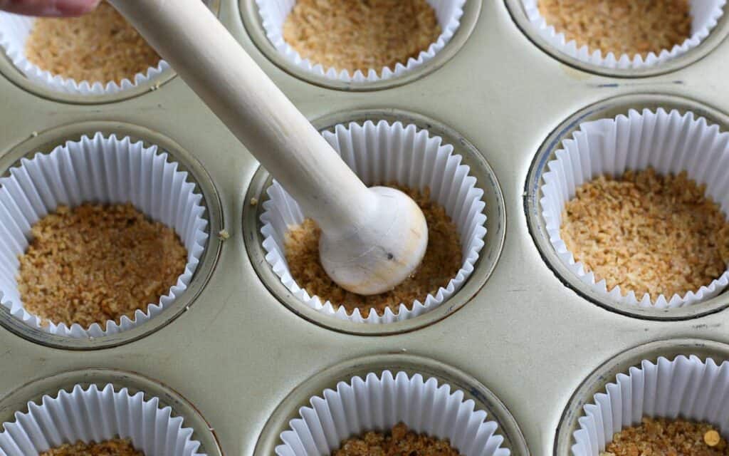 cupcake liners with a stick pressing crumbs into the bottom of each well