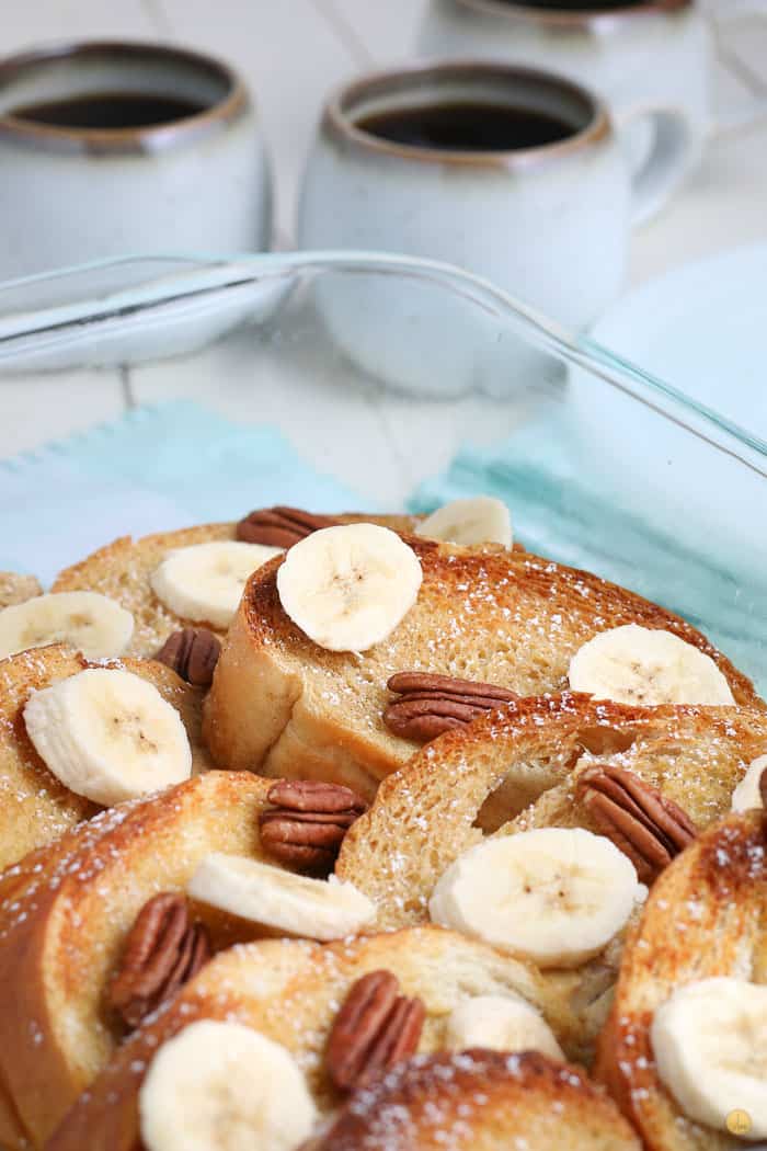 banana pecan oven baked french toast in a clear dish with two cups of coffee