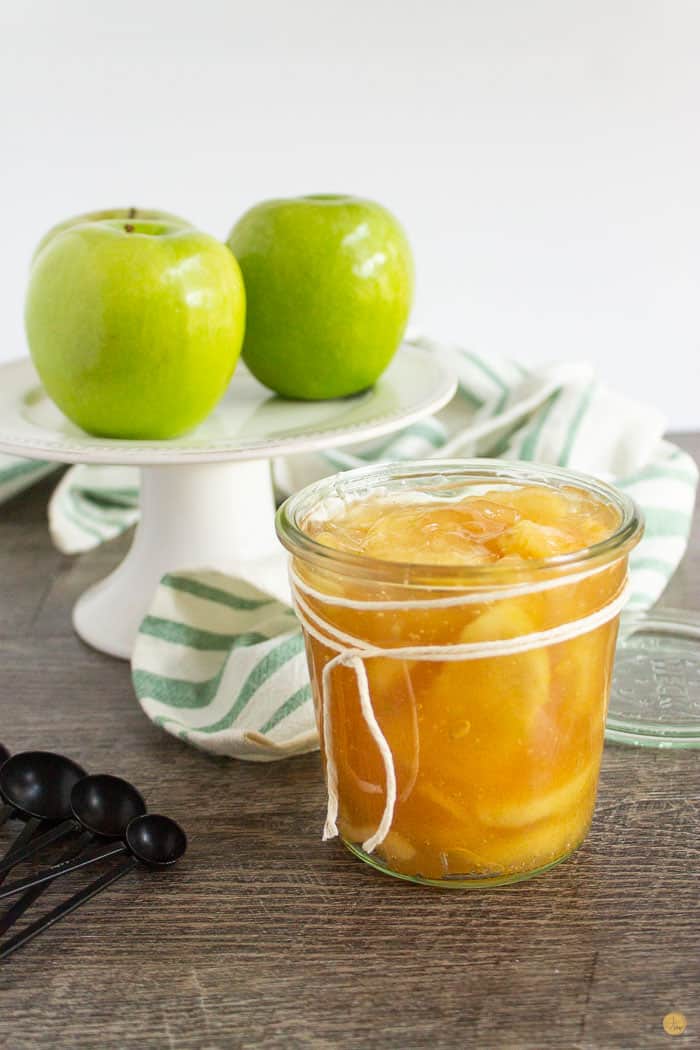 jar of apple pie filling with a cake stand and three apples