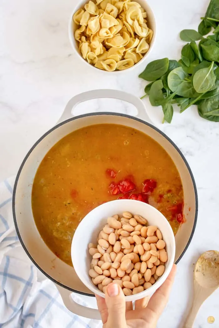 beans and tomatoes being added to soup pot