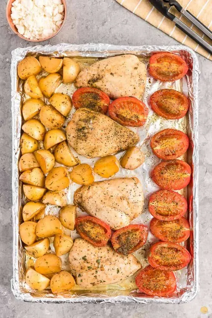 cooked chicken potatoes and tomatoes on a sheet pan