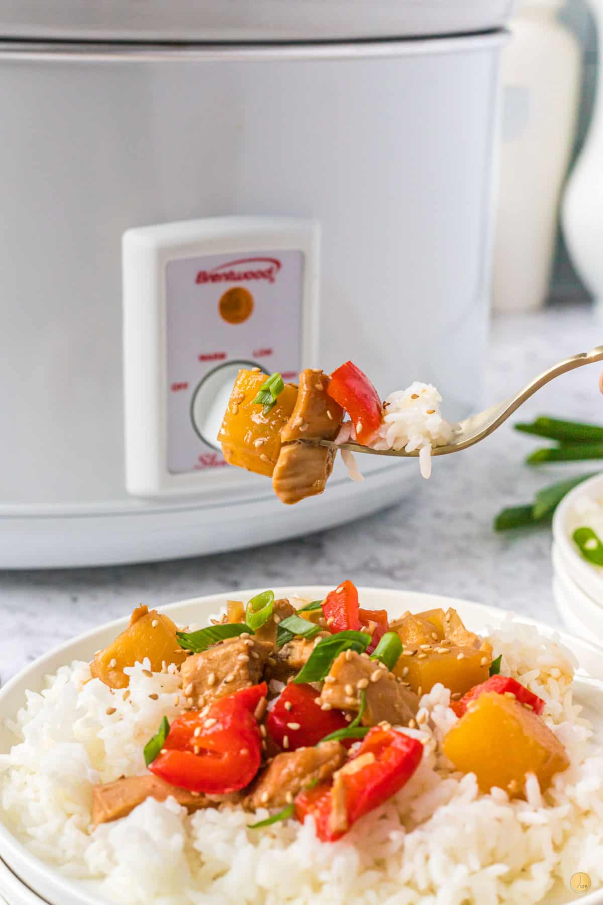 fork of pineapple and chicken over plate of rice