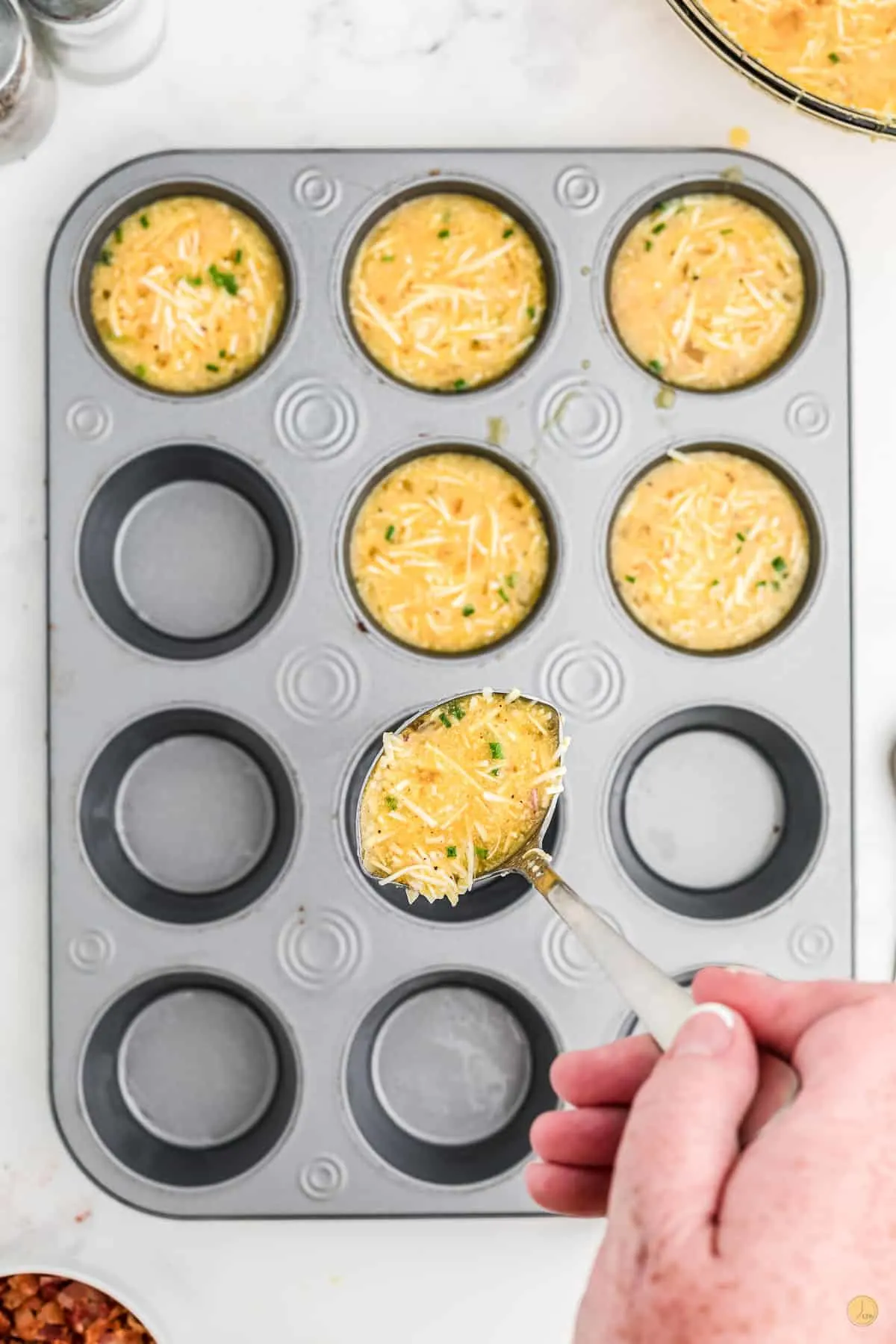 egg mixture being spooned into a muffin pan