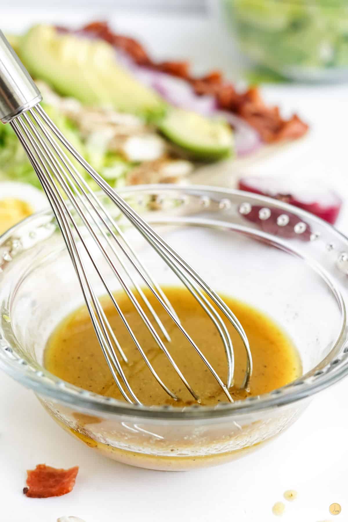 a bowl with salad dressing and a whisk
