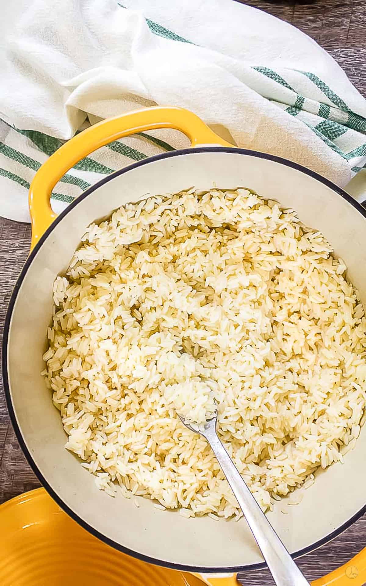 baked white rice in a yellow dutch oven. Fork in the rice and green and white striped napkin on the left