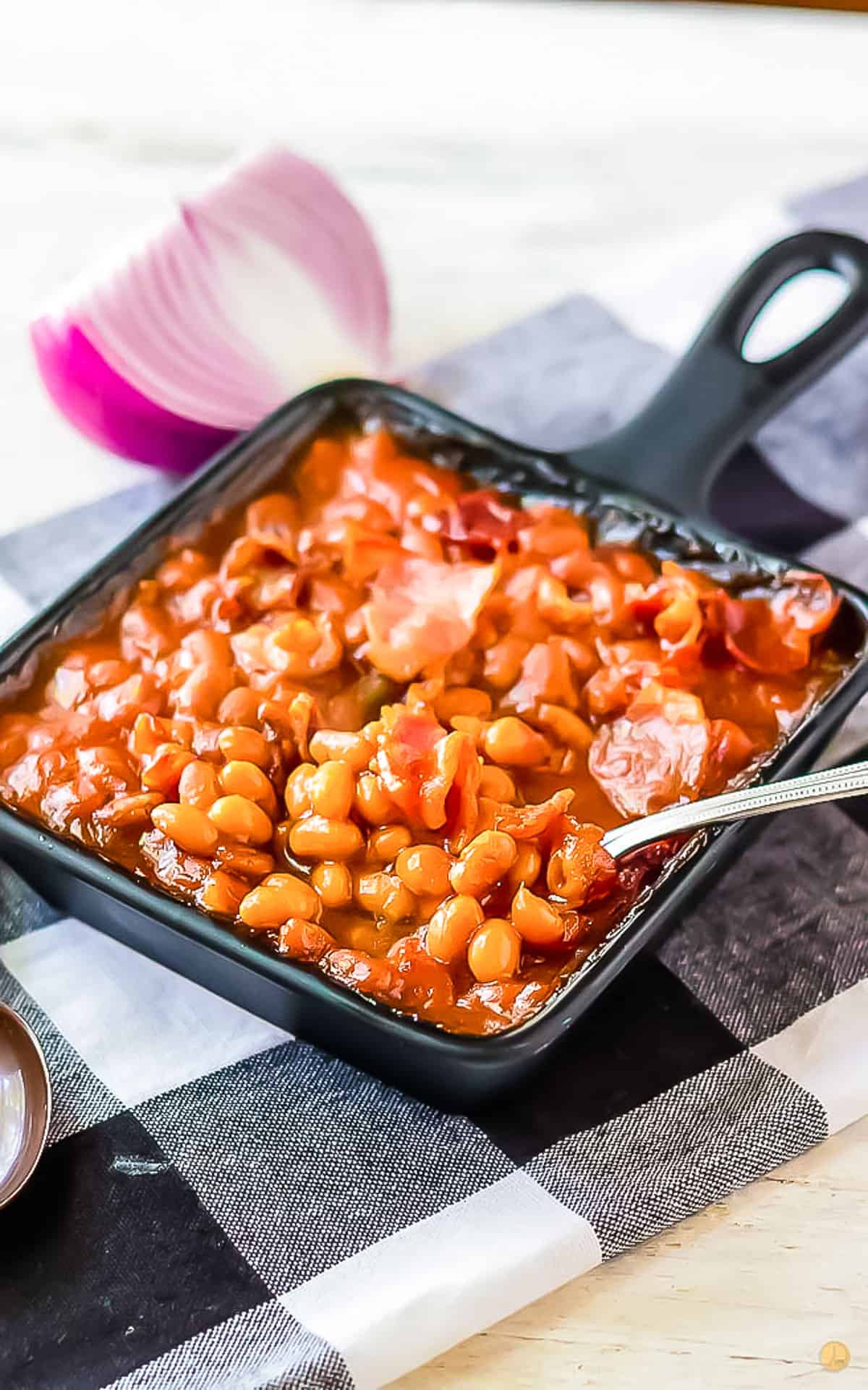 spoon scooping beans out of a square pan on a checkerboard napkin
