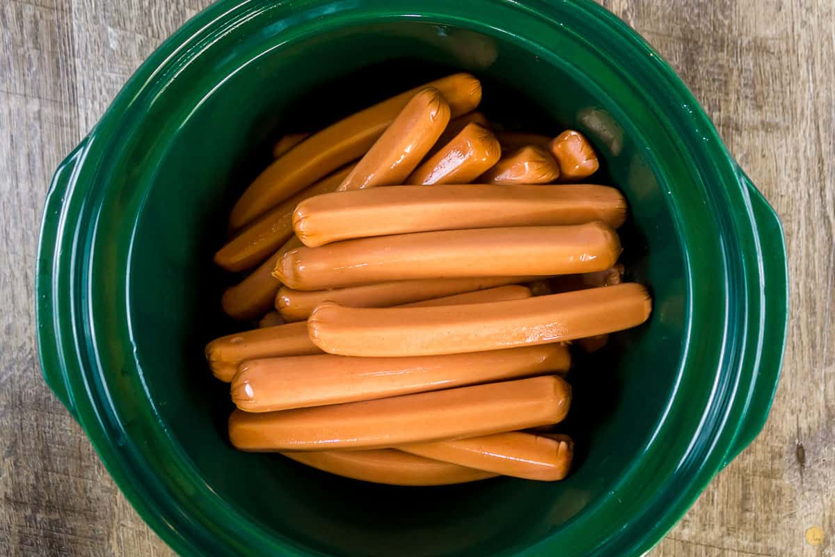 uncooked hot dogs in a green crock pot bowl