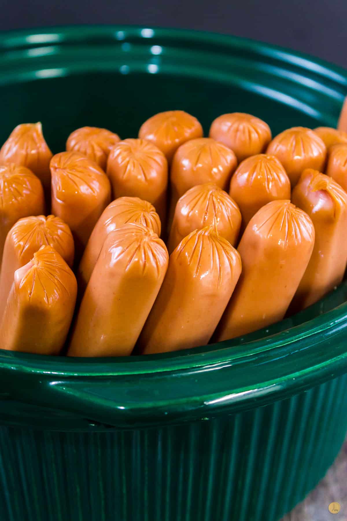 hot dogs standing on end in a green slow cooker bowl