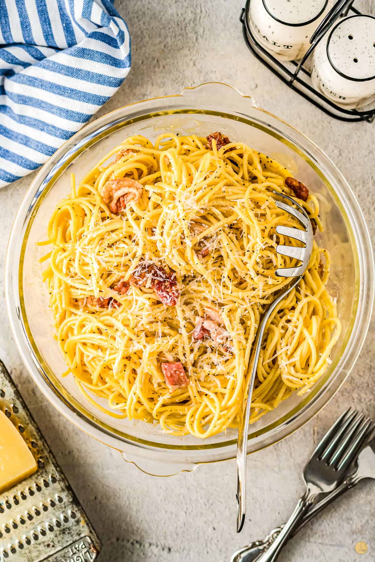 Spaghetti Carbonara in a large glass bowl with a spaghetti spoon in it. 