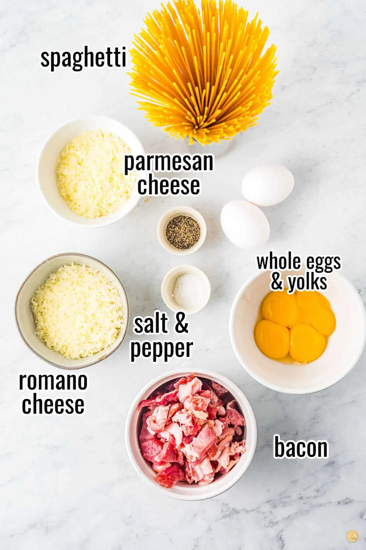 Small white bowls on a marble worktop each containing one of the following ingredients: Spaghetti, Bacon, Eggs, Parmesan cheese, Romano, Salt, and Pepper.