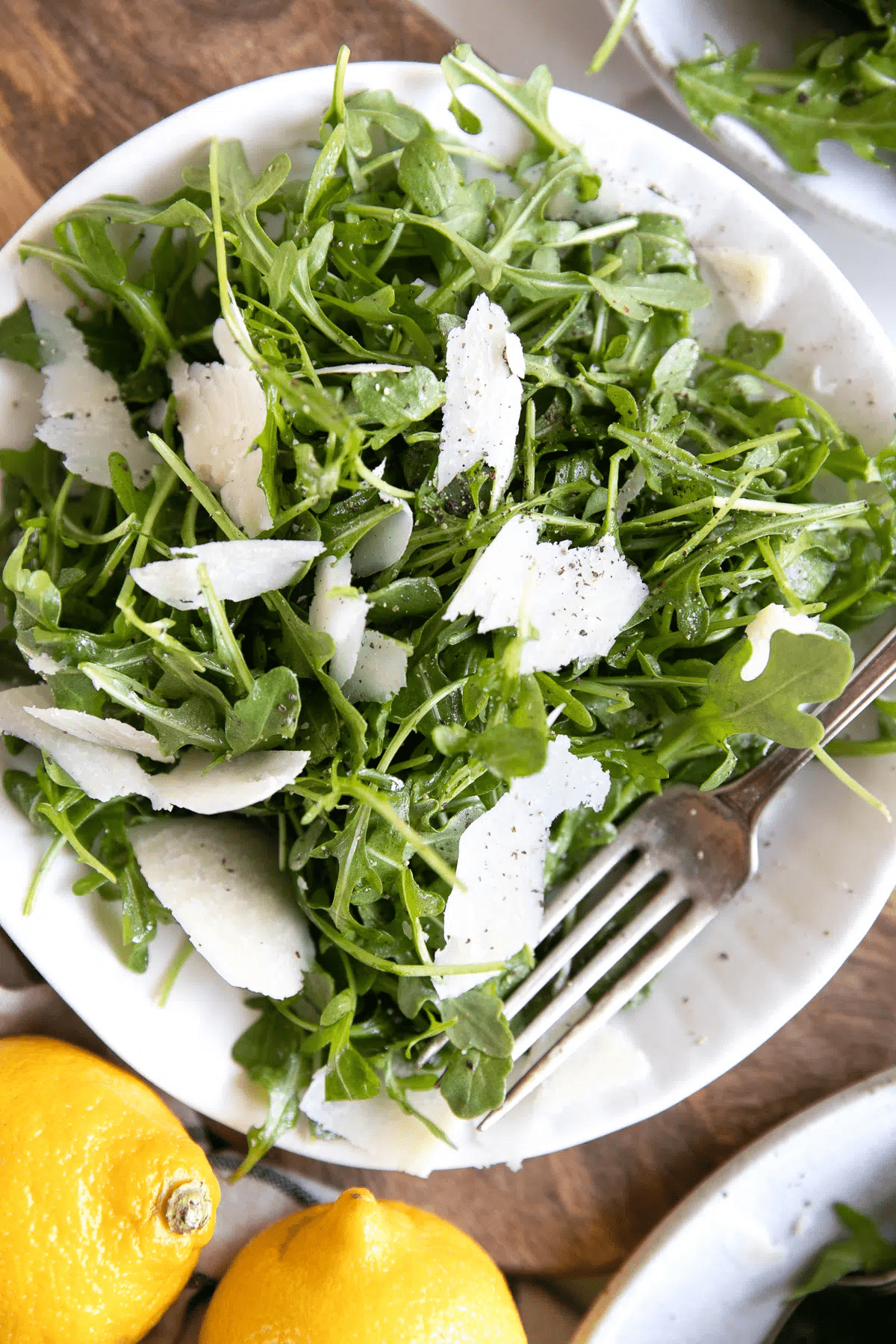 Arugula salad on a white bowl on a table with a fork in it. 