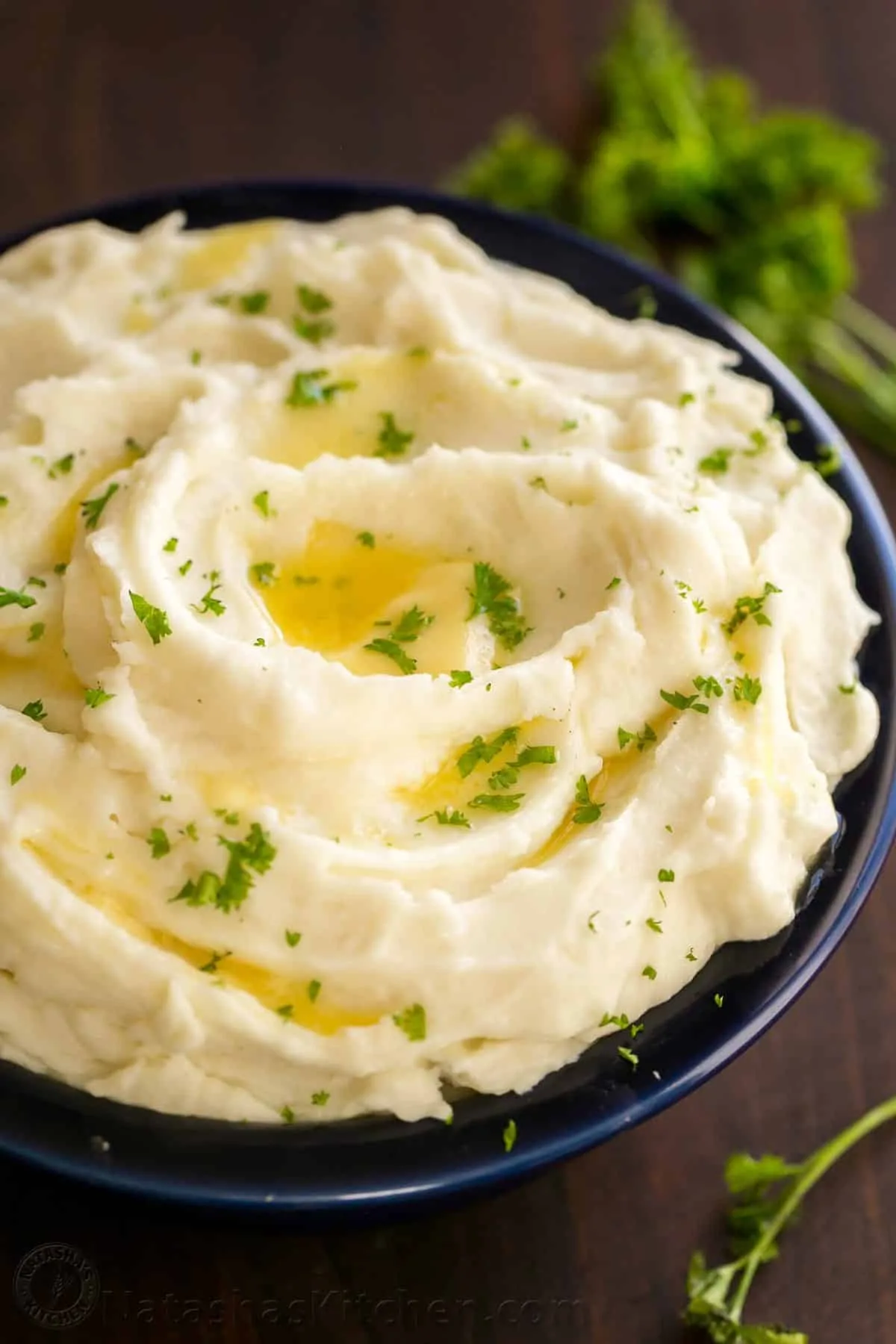 Mashed potatoes in a black bowl on a table with garnish on top.  
