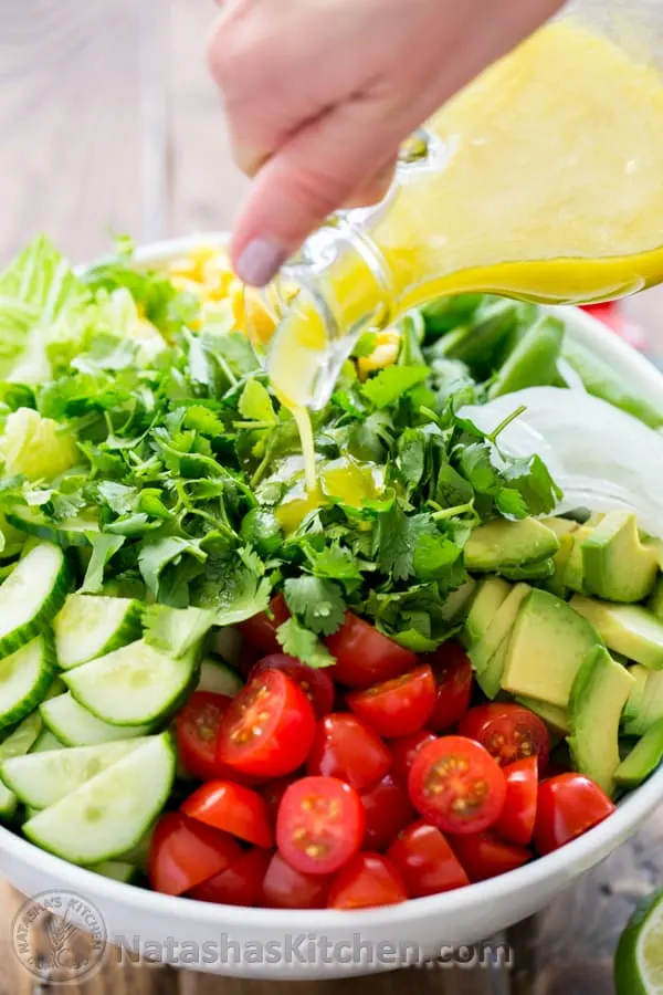 Mexican salad in a bowl with lime dressing being poured on it from a glass bottle. 