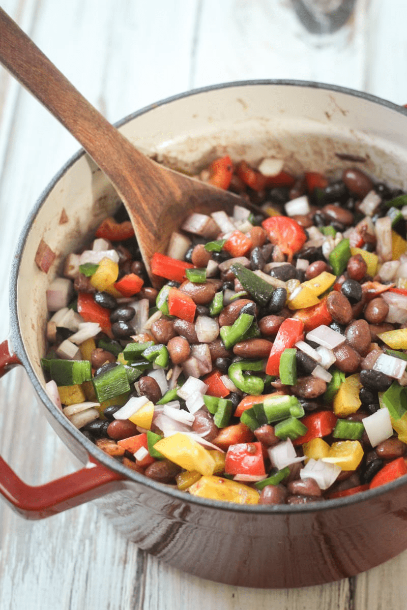 Mexican Three Bean Salad in a big pot and a wooden spoon in it.