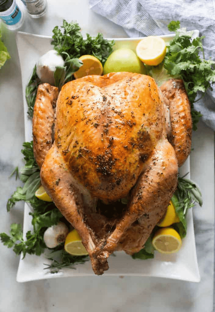 Roasted turkey on a white serving dish surrounded by green salad leaves, lemon and garlic. 