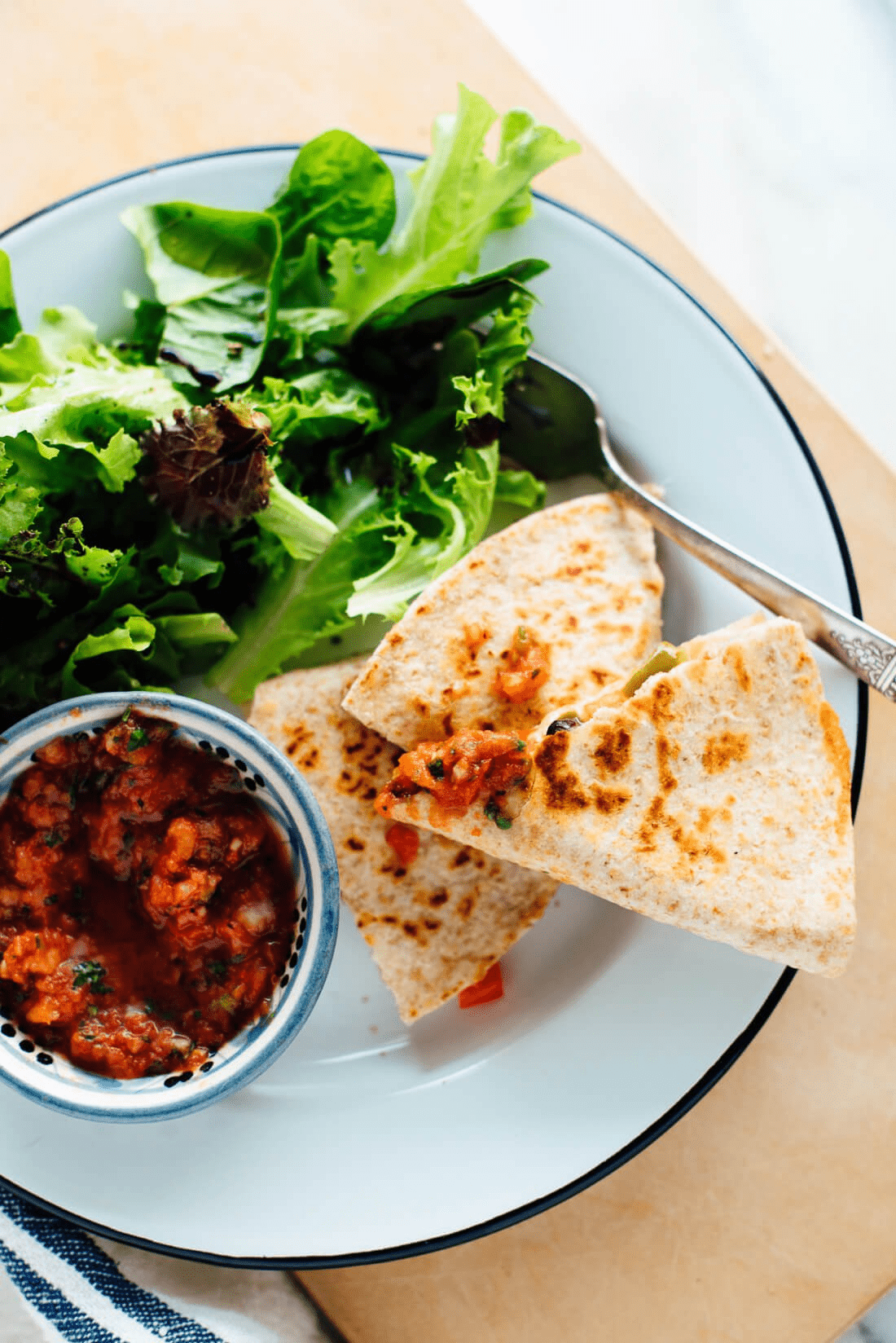 Quesadillas on a white plate with salad and a bowl of salsa. 