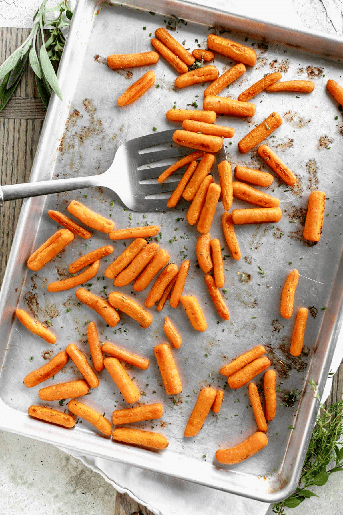Baby carrots, roasted and on a silver tray with a spatula lifting some of them out. 