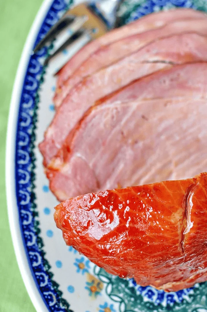 Honey glazed cooked ham cut in slices on a blue and white patterned serving dish. 